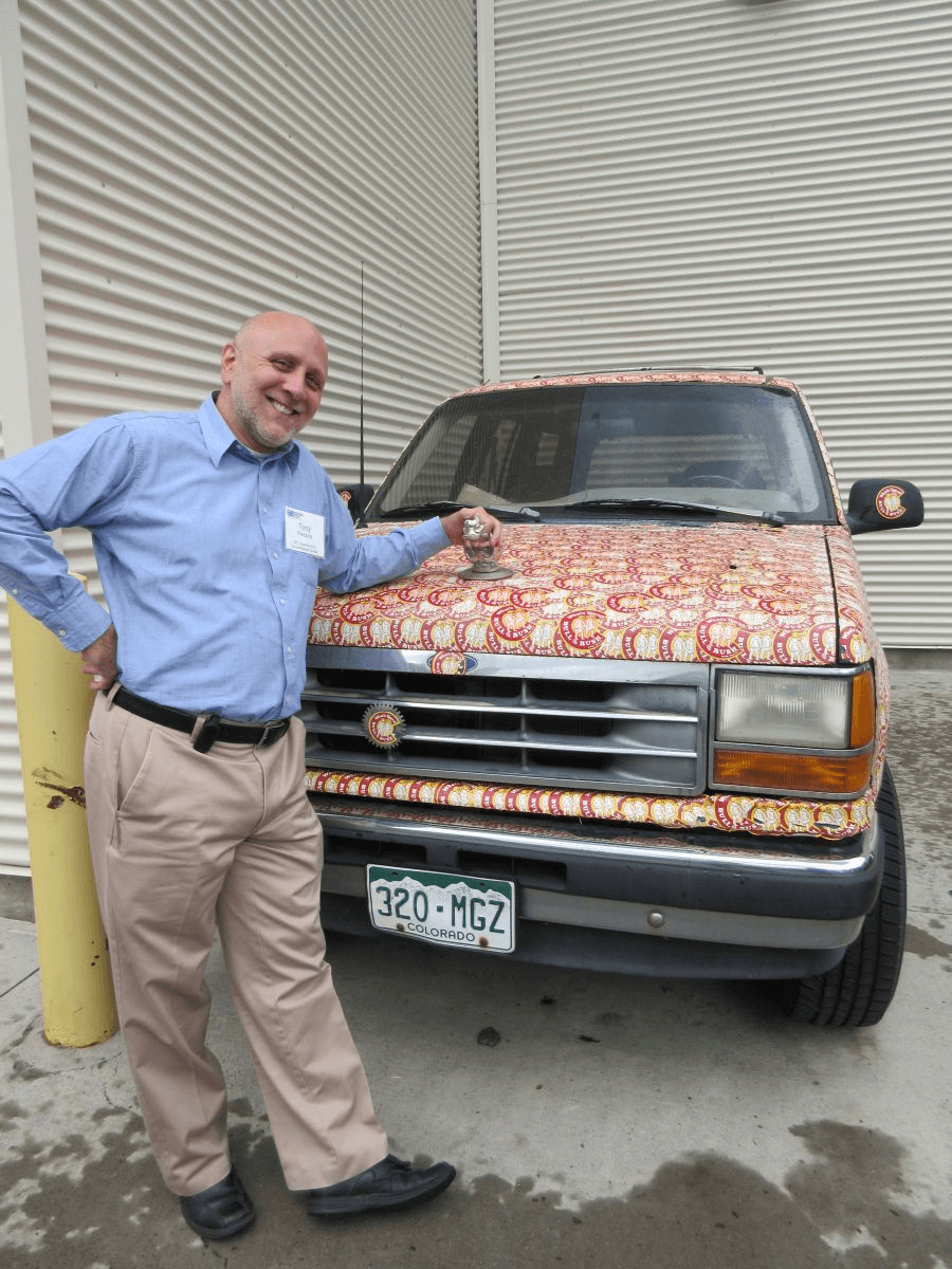 Image of conference attendee next to a car covered with stickers.